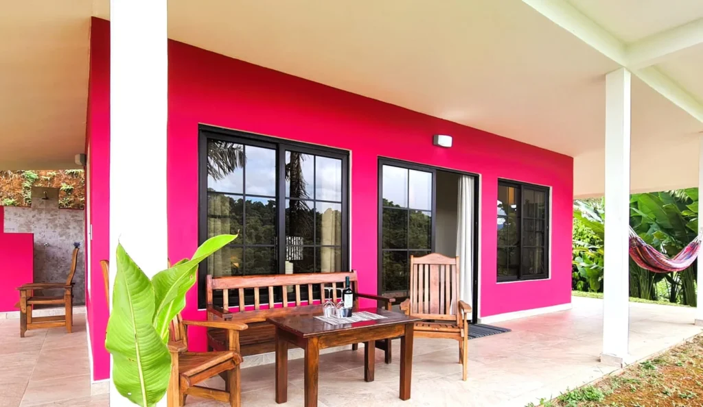 Covered terrace at Casa Rosado with wooden furniture, a pink façade and a hammock