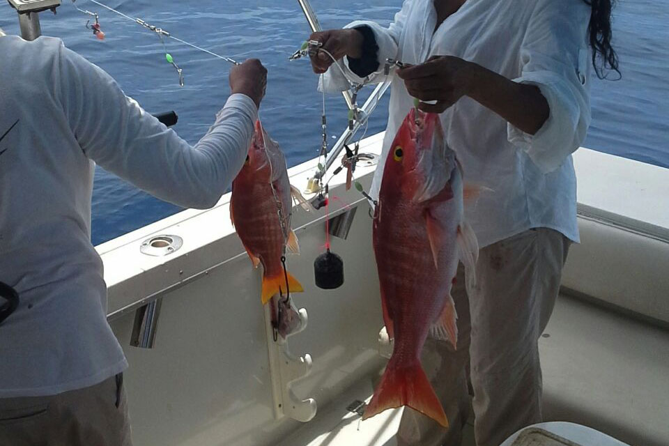 Two people showing freshly caught fish aboard a boat